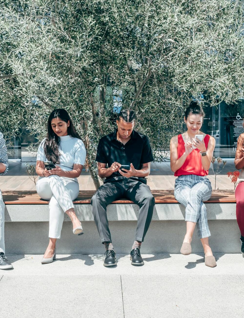 people sitting on a bench using smartphones